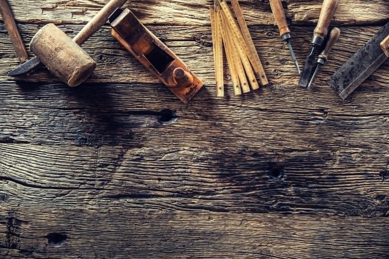 Flat lay of traditional woodworking hand tools including a mallet, hand plane, folding ruler, and chisels