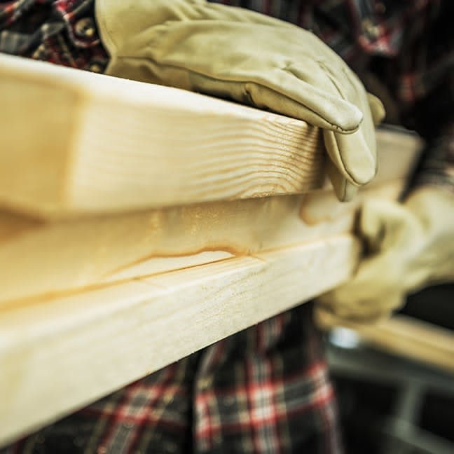 Carpenter in work gloves carefully carrying freshly cut lumber in the workshop