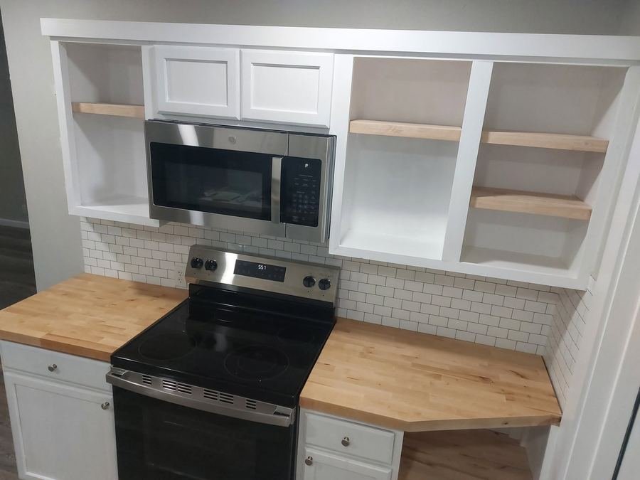 Close view of white kitchen cabinetry with built-in microwave and open shelving